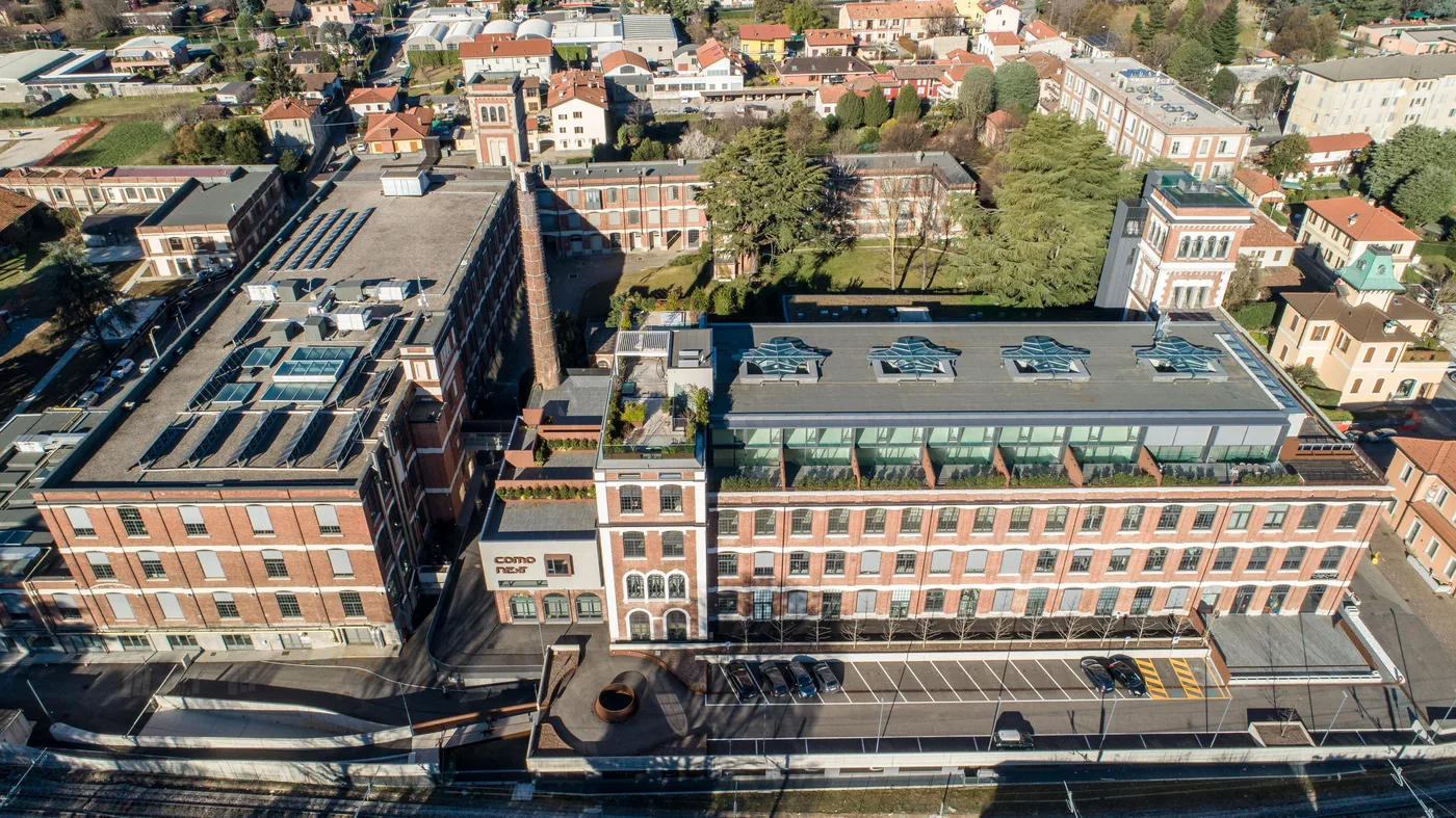 Vista ravvicinata degli edifici in mattoni e della ciminiera di ComoNExT, dall’alto.